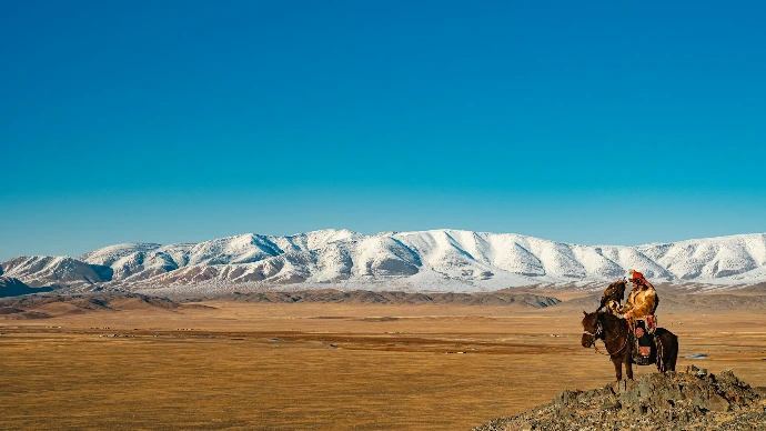 Horse rider overlooks snowy mountains and plains